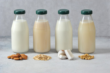 Concept alternative to cow's milk.  Bottles with coconut, oat, soy and almond milk.  Next to the bottles are pieces of coconut, almonds, oatmeal and soybeans.  Light background.  Close-up.