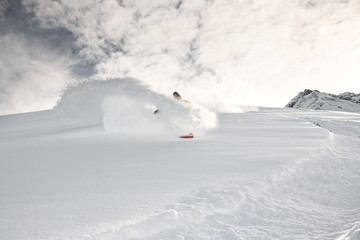 Snowboarder rides through the snow on mountain side