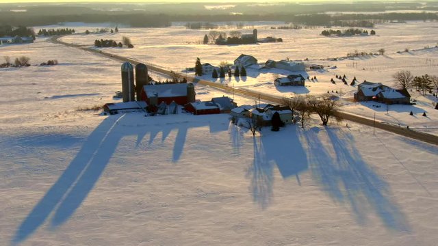 Silos cast long shadows across agricultural landscape, on winter snow, aerial view.