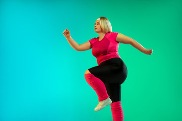 Young caucasian plus size female model's training on gradient green background in neon light. Doing...
