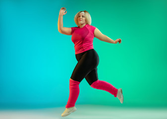 Fototapeta na wymiar Young caucasian plus size female model's training on gradient green background in neon light. Doing workout exercises, stretching, cardio. Concept of sport, healthy lifestyle, body positive, equality.