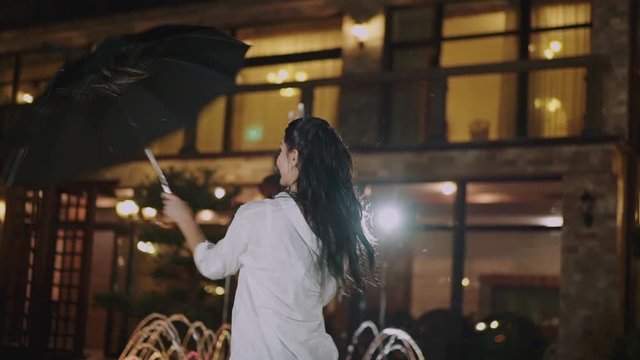 Happy brunette with long hair whirls with umbrella and smiles in night city