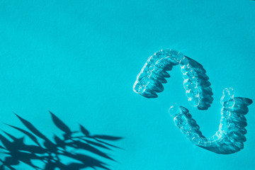 Invisible aligners teeth brackets on blue background with flower shadow