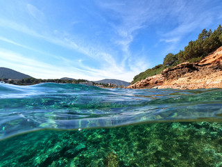 Beautiful underwater split above and below photo of rocky seascape with deep blue sky in tropical...