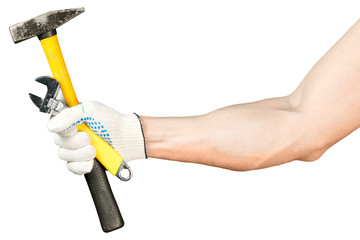 A male hand in a working glove holds a hammer and an adjustable wrench