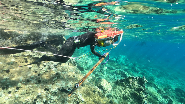 Underwater above and below photo of spear fishing diver in deep emerald exotic paradise bay with caves and rocky seascape