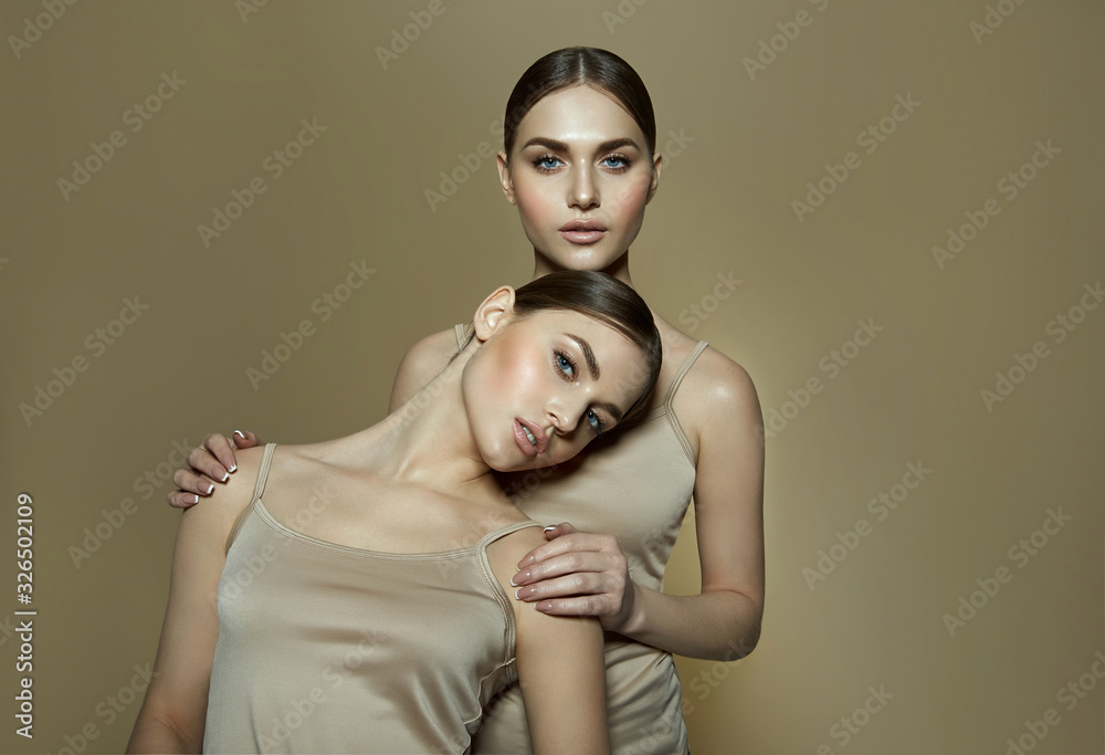 Wall mural beautiful and young twin sisters having fun and laughing in the studio on a beige background in beig