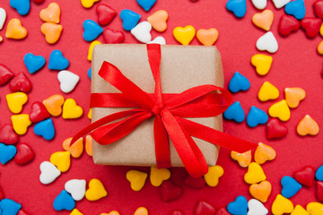 Gift box on a red background with colored hearts. Bright gift. View from above