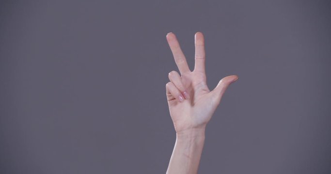 Woman counting on grey background, closeup. Sign language