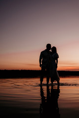 Young couple embracing and kissing in the water on Sunset. Two silhouettes against the sun. Romantic love story.