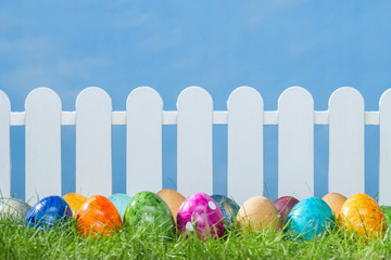Spring grass and wooden fence with easter eggs on cloudy sky