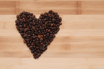 coffee beans laid out in the shape of a heart on a wooden surface. the view from the top