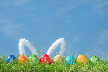 Easter eggs and bunny ears in spring grass with cloudy sky