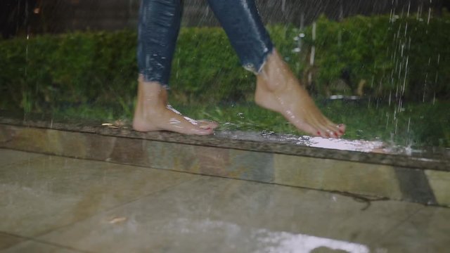 Low view of female bare legs walks on edging under the rainfall