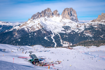 View of a ski resort piste with people skiing in Dolomites in Italy. Ski area Belvedere. Canazei, Italy - obrazy, fototapety, plakaty