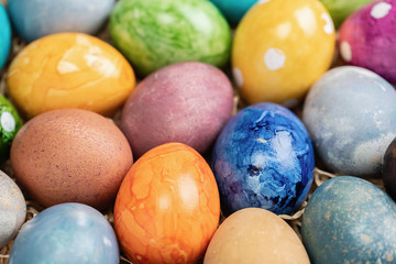 Different easter eggs with straw on wooden plate on green table