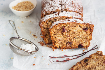 Spicy apple, nuts and dried cranberry loaf cake decorated with powdered sugar on a paper.