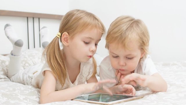 Adorable caucasian children using modern gadget, playing and looking on tablet.