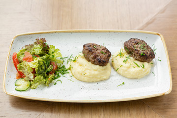 Delicious juicy meat cutlets, mashed potatoes sprinkled with greens and fresh healthy salad of tomatoes and lettuce leaves.