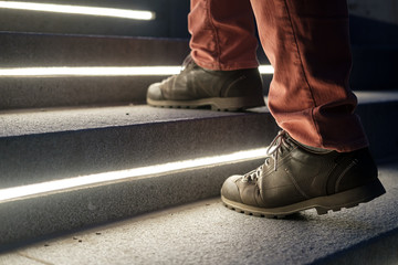 Fototapeta na wymiar Male legs in walking boots climb the lit stone steps on a winter evening.