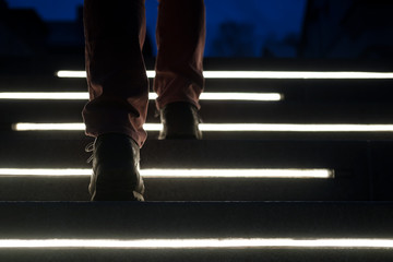 Male legs in boots climb the illuminated stone steps on a winter night. Bottom view.