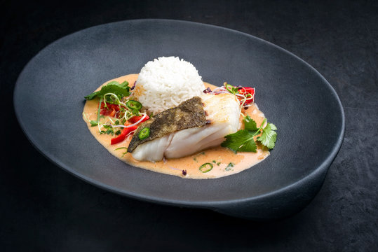 Gebratenes Fisch Filet vom Skrei Kabeljau in Thai Fisch Curry mit Jasmine Reis und Chili als closeup auf einem Modern Design Teller mit Textfreiraum