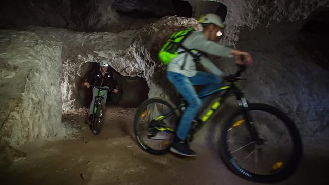 Wide angle shot of young boys mountain biking through a underground cave path. slowmotion. Mežica, Slovenia