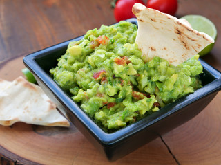 Avocado dip in black square bowl on wooden chopping board.Mexican guacamole spread.