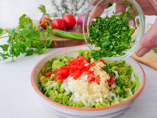 Chef's hand adds freshly chopped cilantro to avocado dip. Making guacamole with ingredients on table