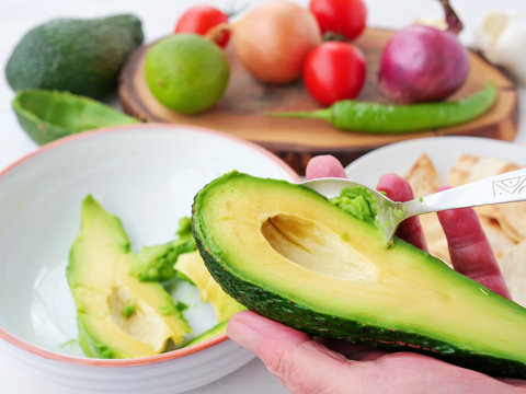 Chef holds half of a pitted avocado in his hand and scoops it out from the skin with a spoon.