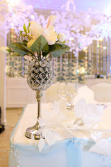 Beautiful vase with flowers on a table with a white tablecloth. Wedding becor on the table