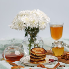Appetizing pancakes are poured with fragrant honey on the table with tea, dried fruits and nuts.