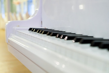 White lacquered piano and piano keys against the background of the hall.