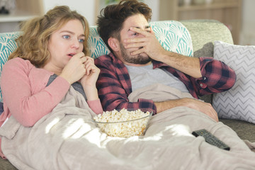 funny couple sitting on sofa watching horror movie