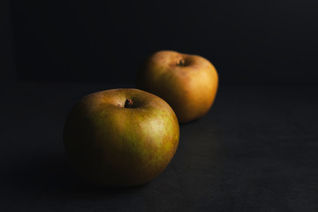one apple behind another with side light on dark background