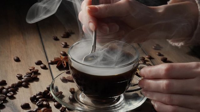 Mixing steaming coffee in a cup with a spoon