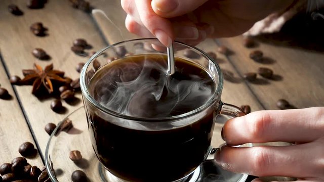Mixing steaming coffee in a cup with a spoon