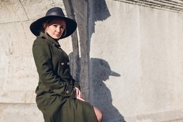 Portrait of stylish young woman in military coat, hat outdoors. Spring fashion female clothes accessories.