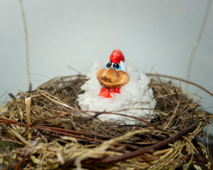 Toy hen sits in a real bird's nest of grass