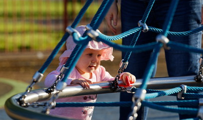 Obraz premium Child playing at playground with her mum, Cute 3 year old baby excitedly plays on playground on a cool sunny day, little girl having fun on outdoor playground. Summer active sport leisure for kids.