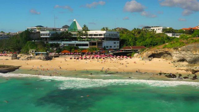 Dreamland beach one of the most beautiful sand beach Bali with happy travel tourist resting under umbrella and surfers in crystal clear sea water. Aerial view. Shot in 4K on Hasselblad, H.265