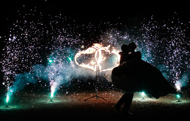 fire show at wedding  party. burning fire heart. romantic loving couple date on  night lights background . Silhouette a groom and bride at night on fire backgroung. wedding background close up