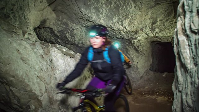 People mountain biking towards the camera in a underground cave. Slowmotion action. Mežica, Slovenia