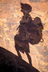 Full length shadow of hiker walking along the incline of a red rock mountain