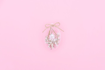 Easter minimal composition with transparent glass egg filled with white flowers on pink background. Eco Stylish decor concept. Copy space. Festive flat lay greeting card