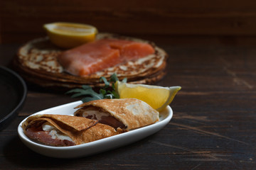 thin pancake roll with weak salt salmon and cream cheese close-up, on a dark background