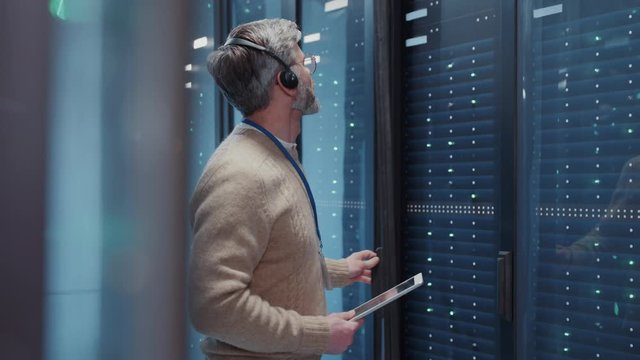 IT operators manager wearing headset for commands examining system security in server cabinet for maintenance working at data center.
