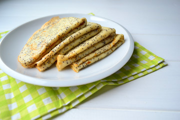 Traditional Russian pancakes with poppy seeds on a white plate with a green napkin. Blini for Maslenitsa.