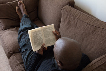 Black man, of African ethnicity, reading on the sofa