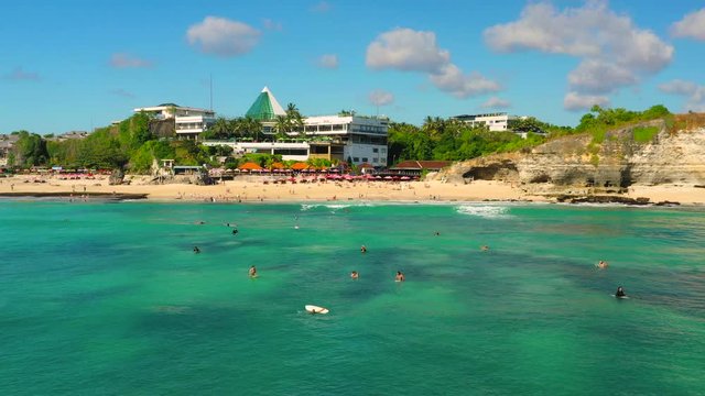 Dreamland beach one of the most beautiful sand beach Bali with happy travel tourist resting under umbrella and surfers in crystal clear sea water. Aerial view. Shot in 4K on Hasselblad, H.265